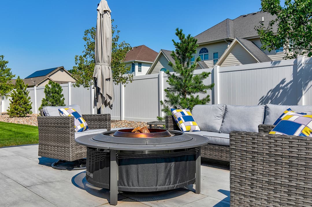 Cozy outdoor sitting area with fire pit, comfortable furniture, and sunny backyard landscaping.