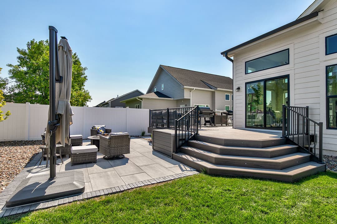 Stylish outdoor patio with seating area, stairs, and modern fencing on a sunny day.
