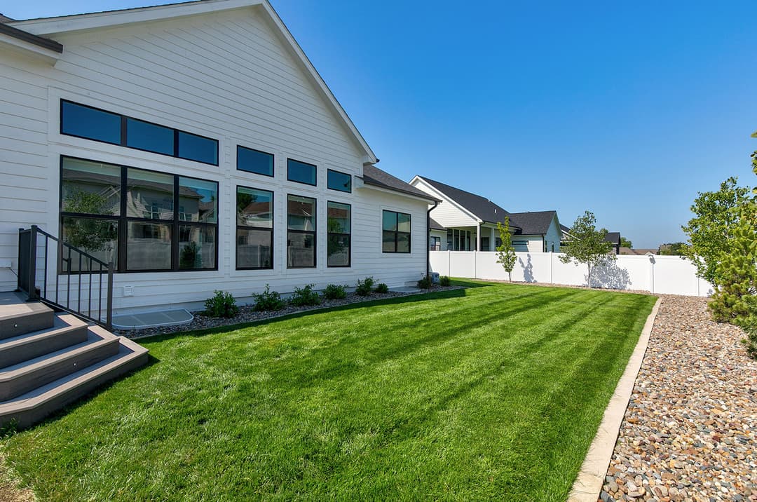 Modern home exterior with large windows, manicured lawn, and white privacy fence on a clear day.