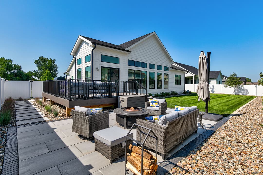 Modern backyard with patio, seating area, fire pit, lush lawn, and sunlit deck.