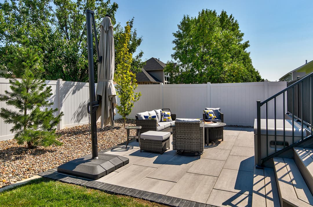 Cozy outdoor patio with seating, table, and lush greenery in a sunny backyard setting.