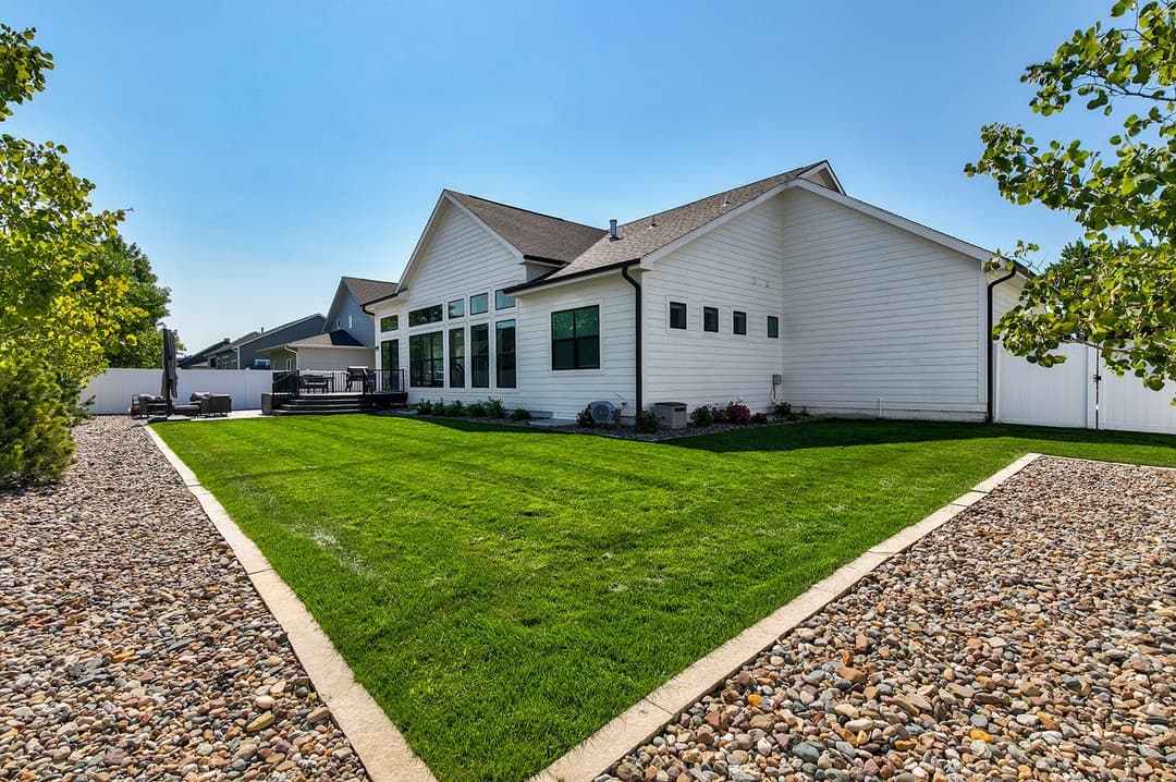 Spacious backyard with manicured grass and gravel pathways beside a modern white house.