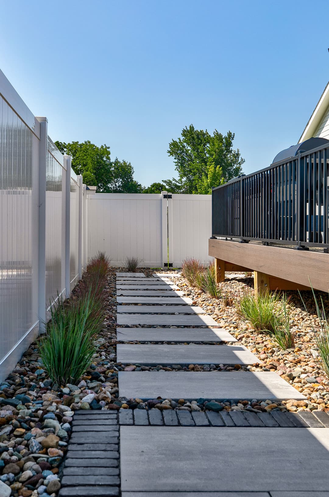 Modern garden pathway with pavers, decorative gravel, and lush greenery alongside a fence.