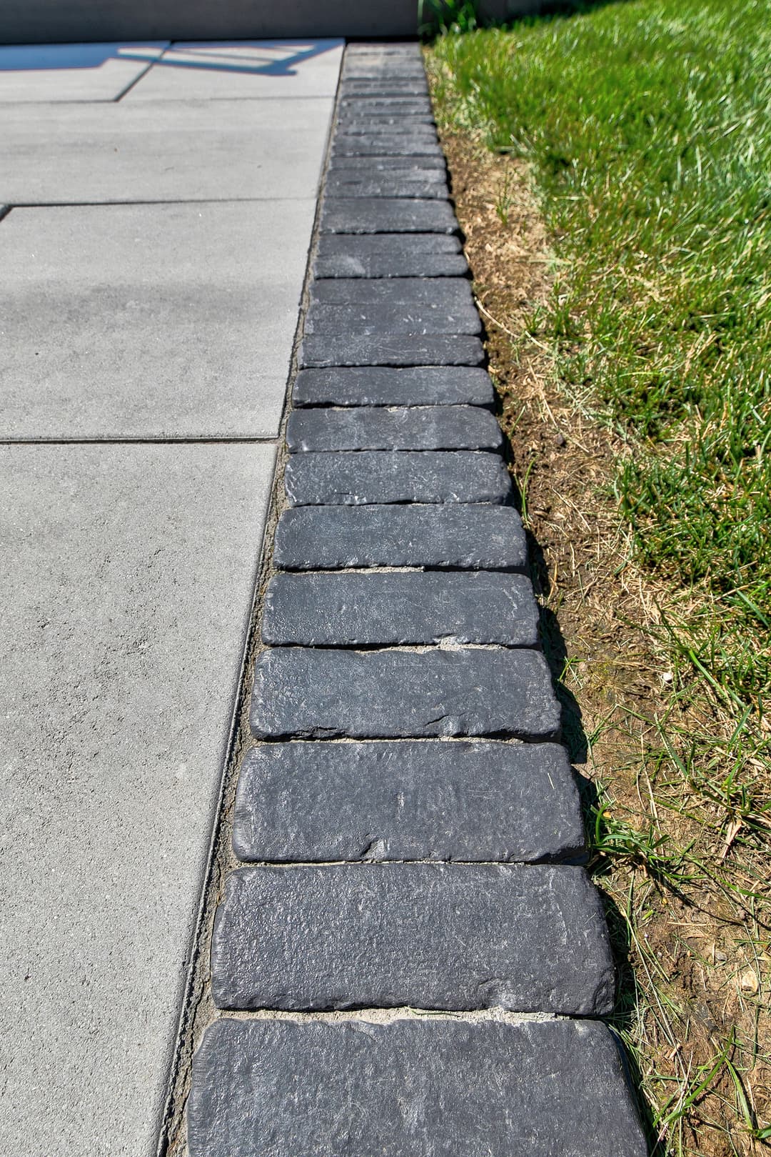 Gray cobblestone edge alongside a concrete walkway and green grass.