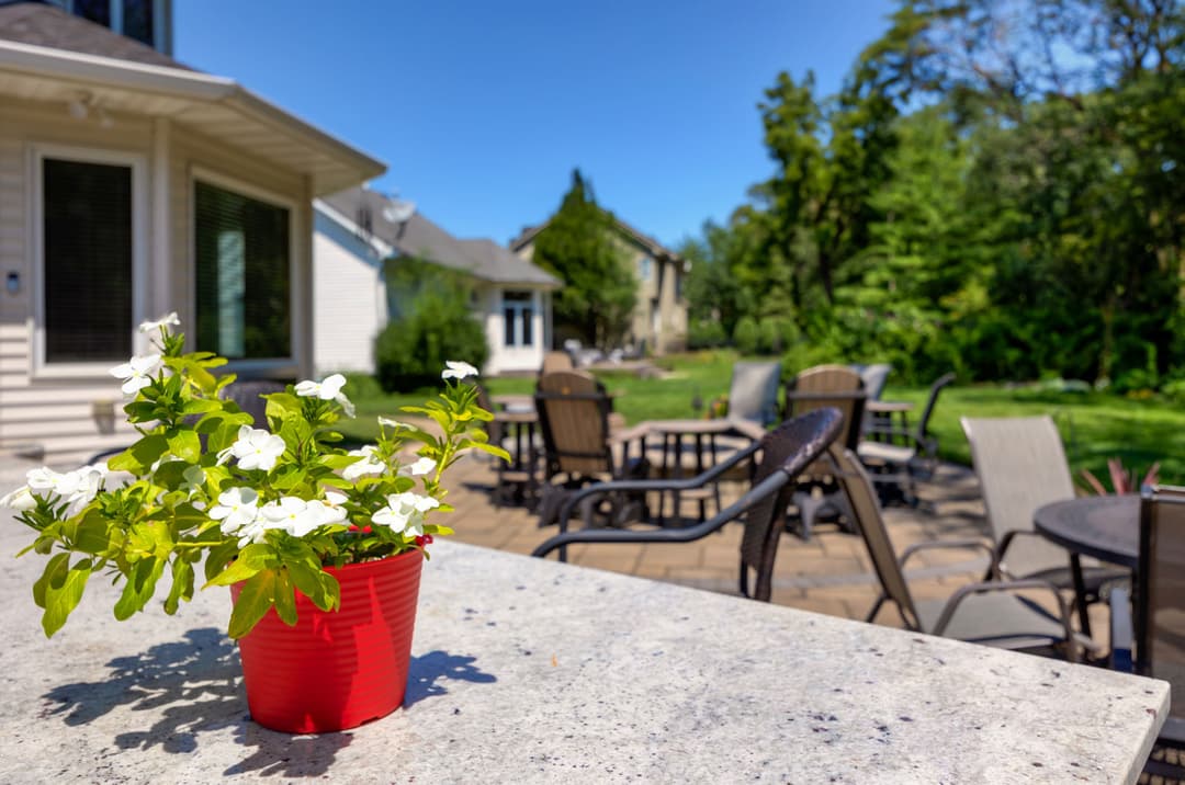 Red pot with white flowers on a stone table, overlooking a sunny patio and garden.