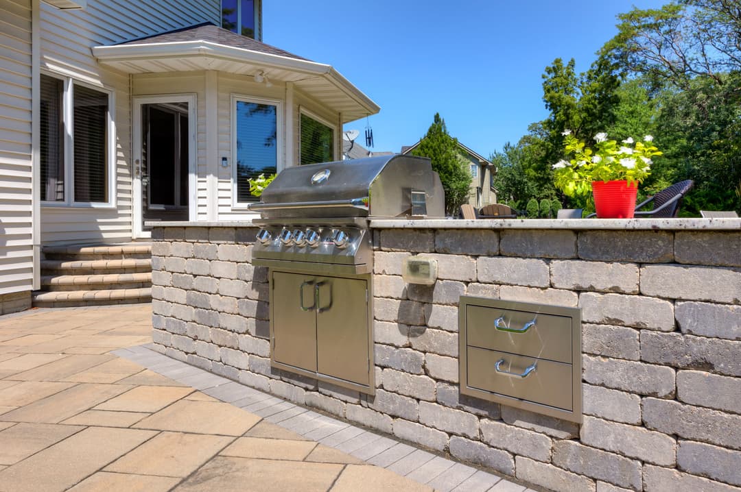 Outdoor kitchen featuring a stainless steel grill and stone countertop, surrounded by a patio.