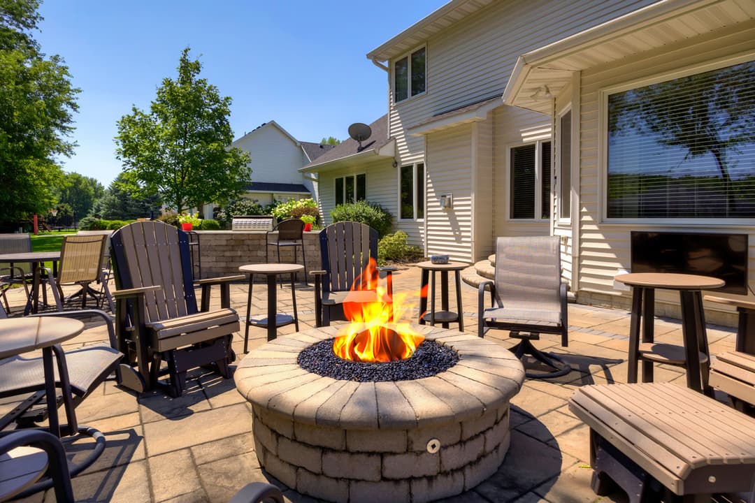 Cozy outdoor fire pit surrounded by chairs in a sunny backyard setting. Ideal for gatherings.