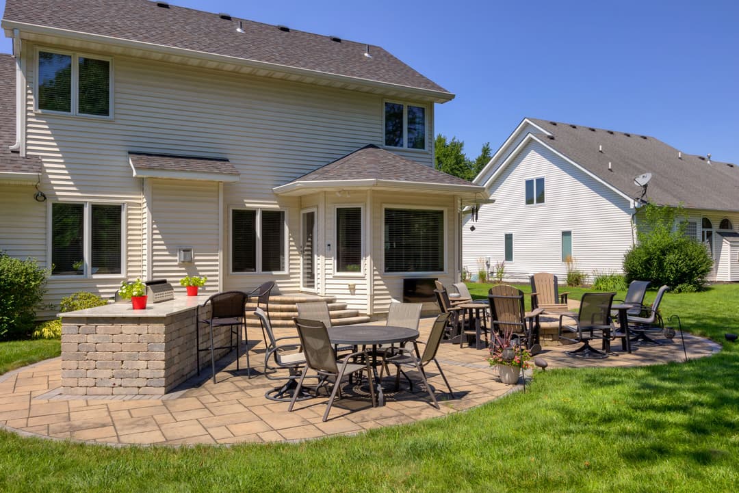 Backyard patio with seating, stone fire pit, and modern home exterior on a sunny day.