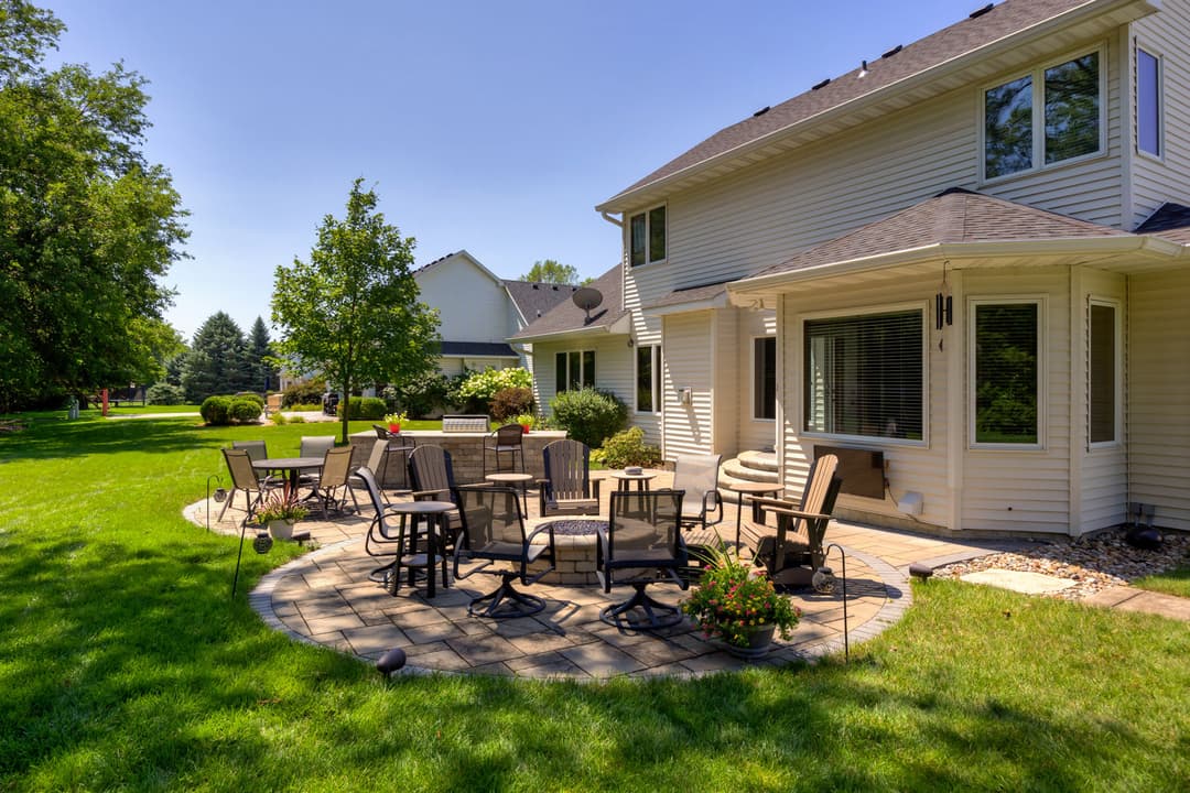 Spacious backyard patio with seating, surrounded by lush green grass and trees. Perfect for relaxation.