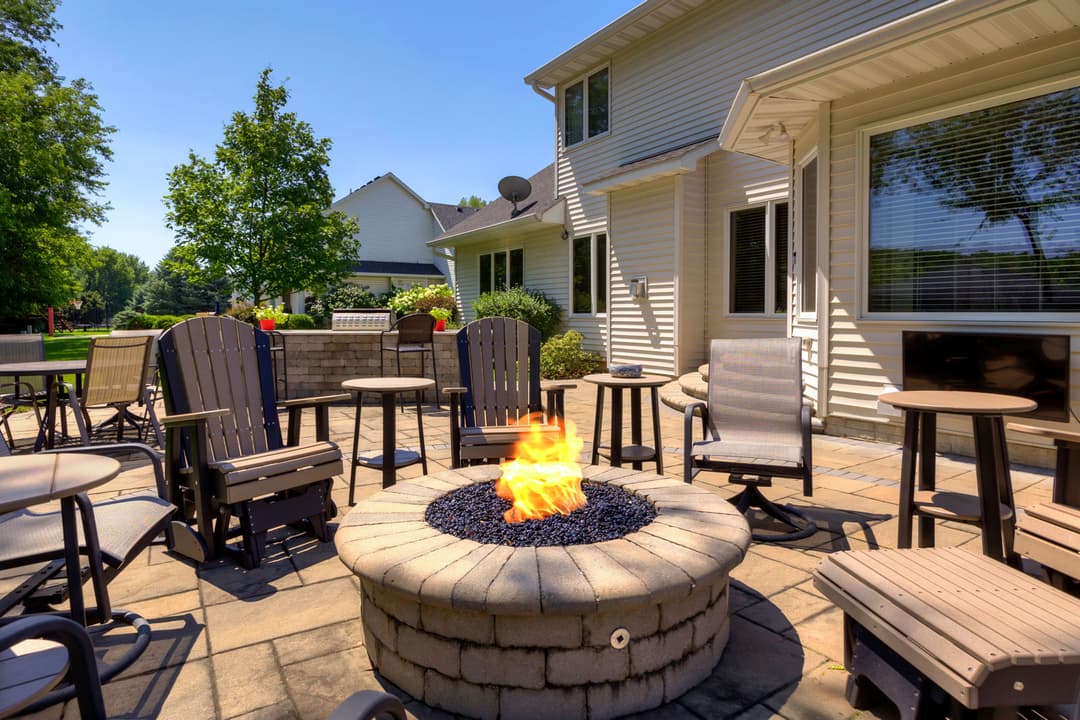 Cozy outdoor fire pit surrounded by chairs in a sunny backyard setting.