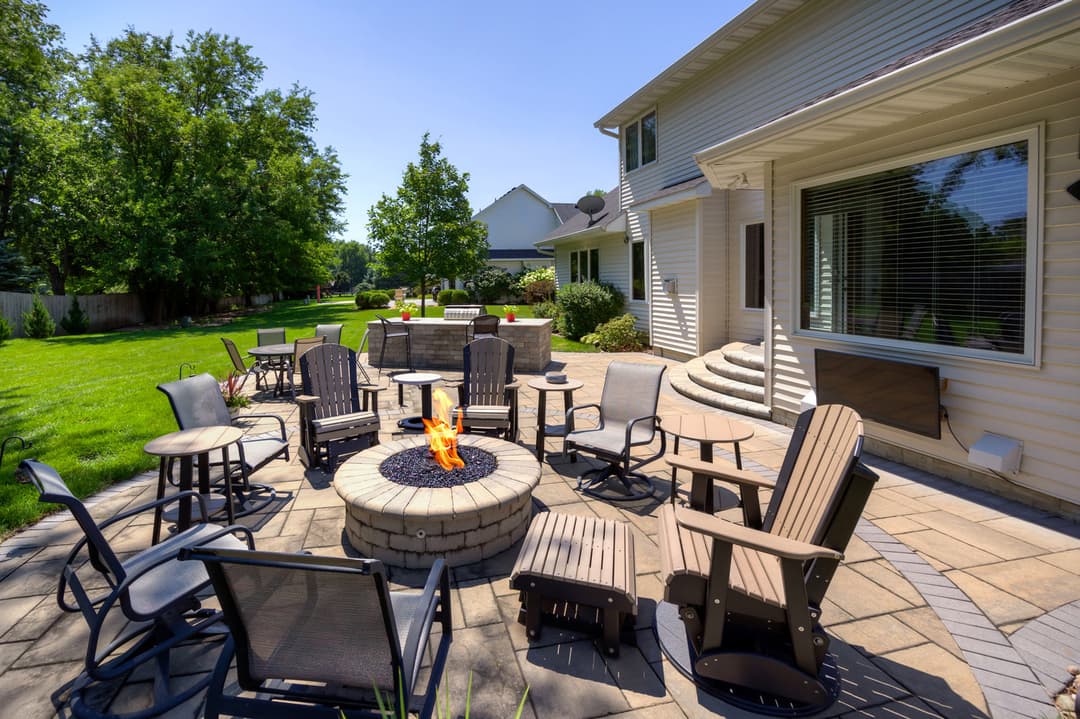 Cozy backyard patio with fire pit, seating, and lush greenery on a sunny day.