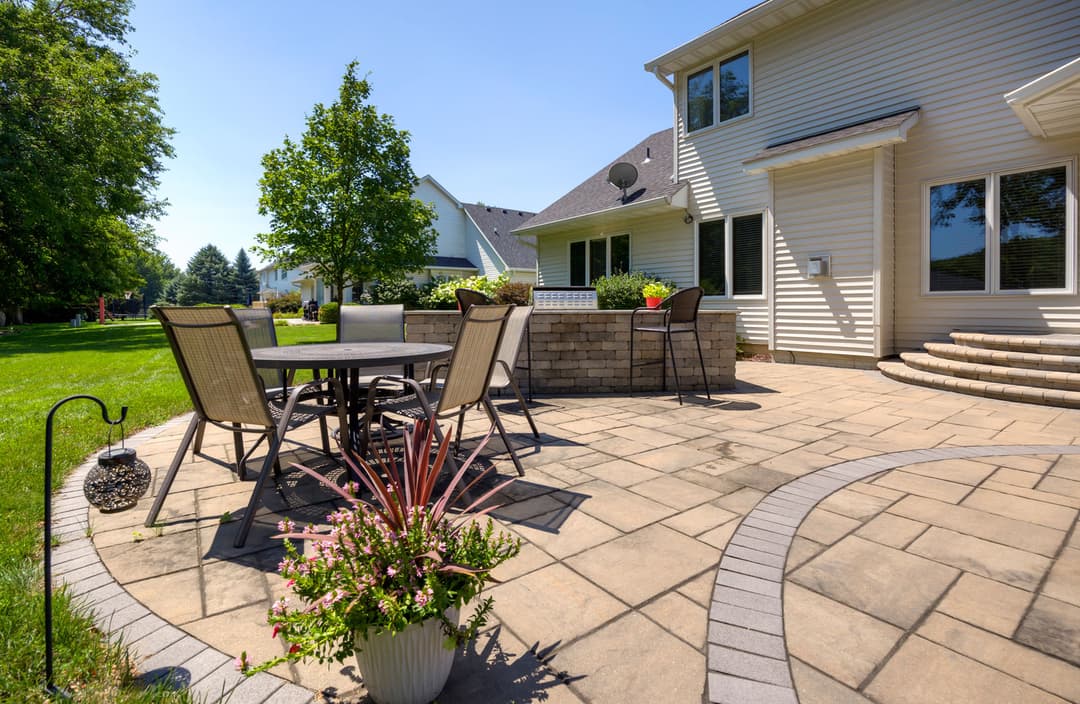 Sunny backyard patio with dining set, landscaping, and stone features. Perfect for outdoor gatherings.