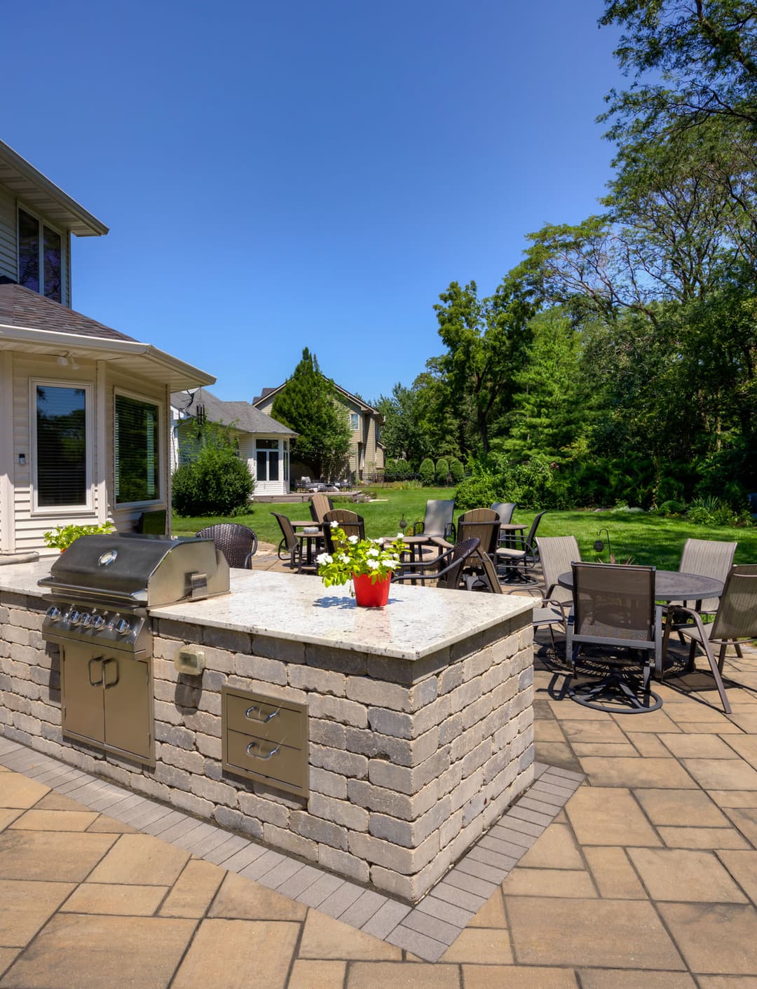 Outdoor patio with a stone grill, dining furniture, and lush greenery in the background.