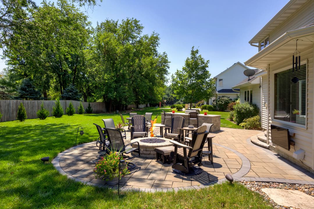 Cozy backyard patio with fire pit, seating, and lush green lawn under clear blue sky.
