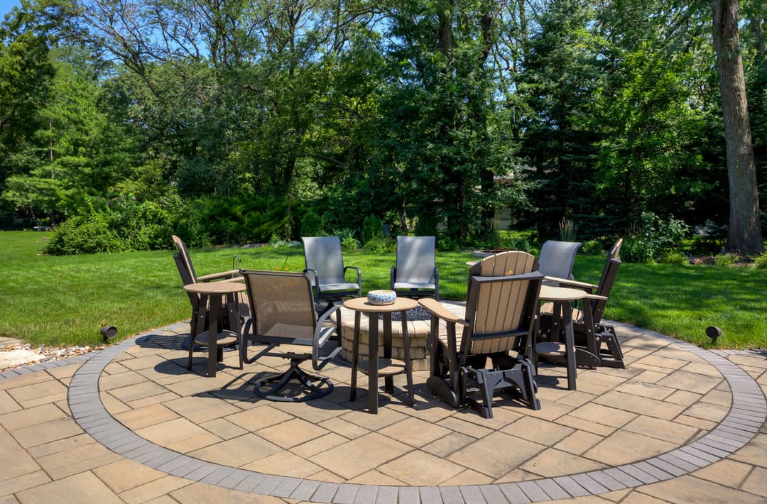 Outdoor patio with seating area, fire pit, and lush green landscaping in a sunny garden.