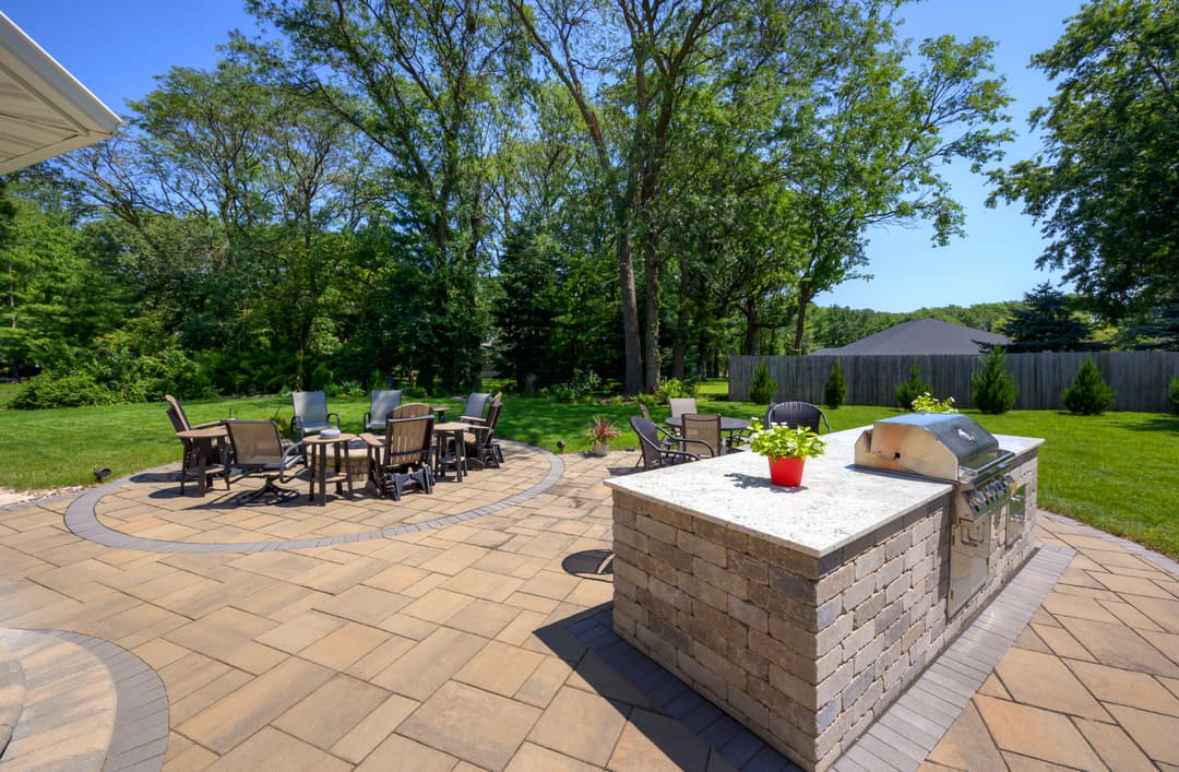 Stylish outdoor patio with a grill, dining area, and lush green surroundings.