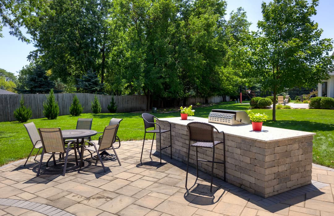 Outdoor patio with grill and seating area surrounded by lush greenery. Perfect for gatherings.