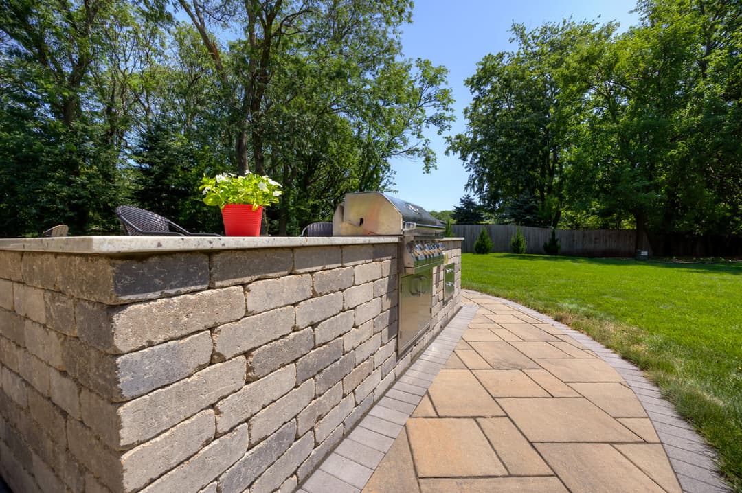 Modern outdoor kitchen with grill and planters in a spacious green backyard setting.