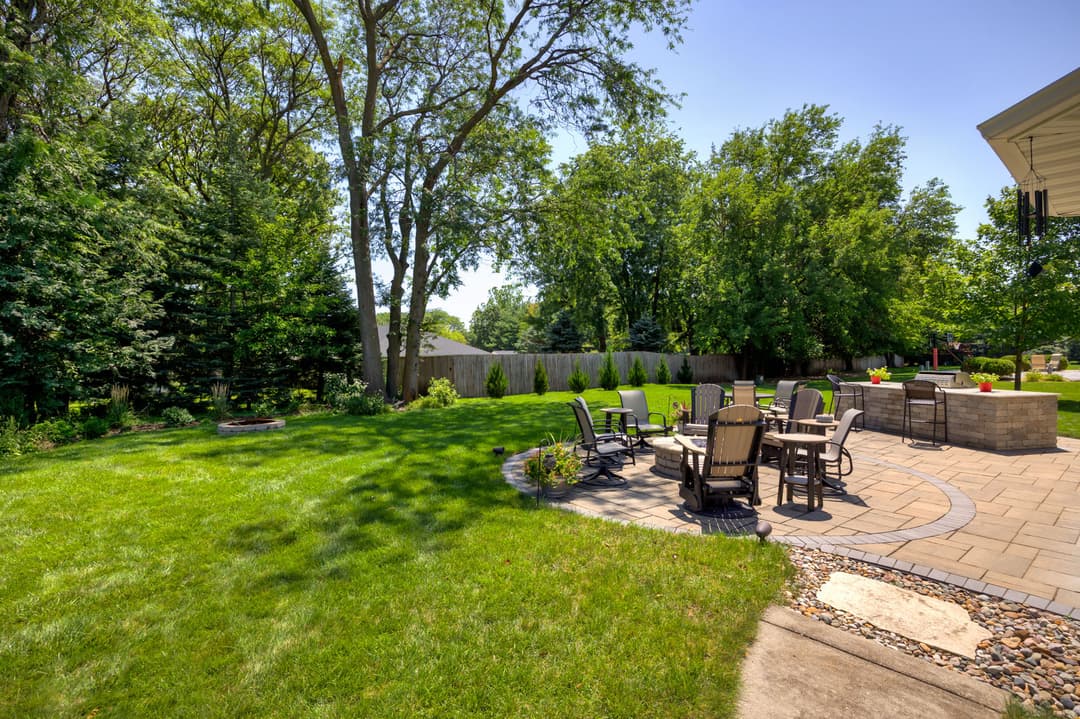 Spacious backyard with patio furniture, green lawn, and trees under a clear blue sky.