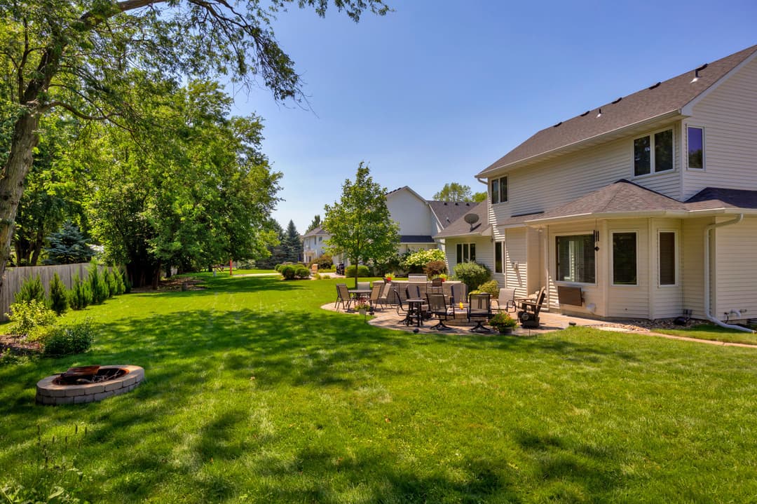 Lush backyard with patio, fire pit, and greenery in a residential neighborhood.