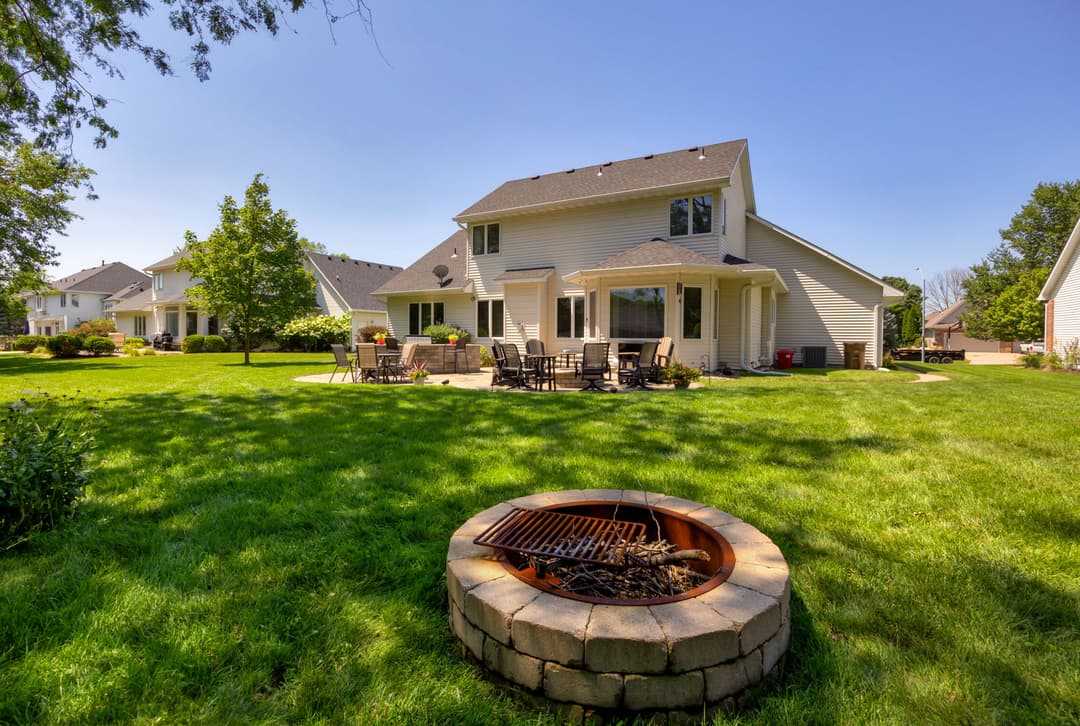 Backyard with a fire pit, patio furniture, and a modern home surrounded by green lawn.