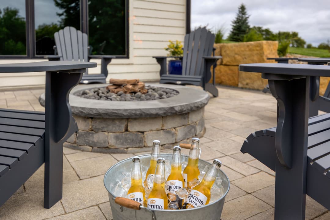 Chilled Corona beers in a bucket beside a fire pit and outdoor seating furniture.