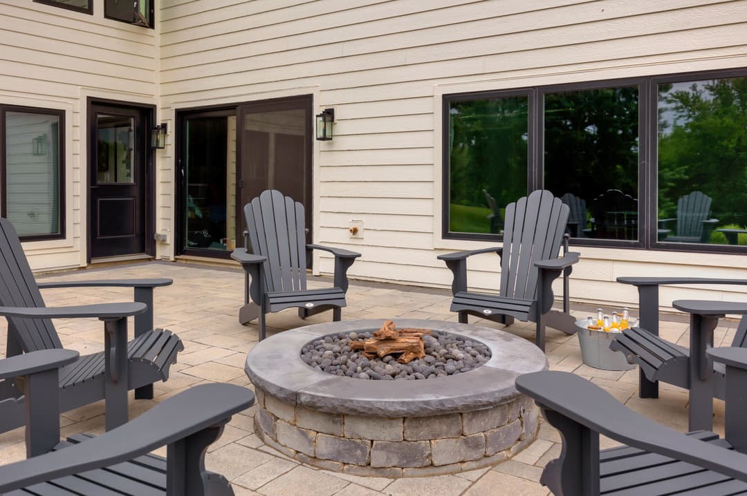 Cozy outdoor patio with gray Adirondack chairs and a stone fire pit surrounded by greenery.