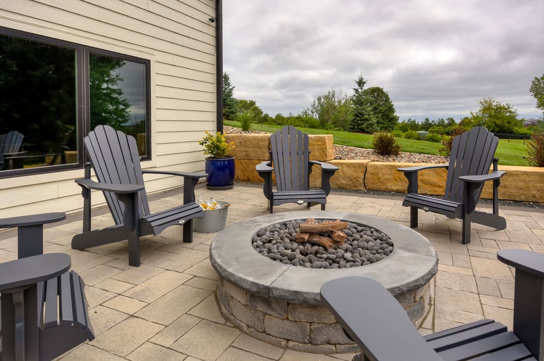 Cozy outdoor patio with Adirondack chairs around a fire pit and scenic green landscape.