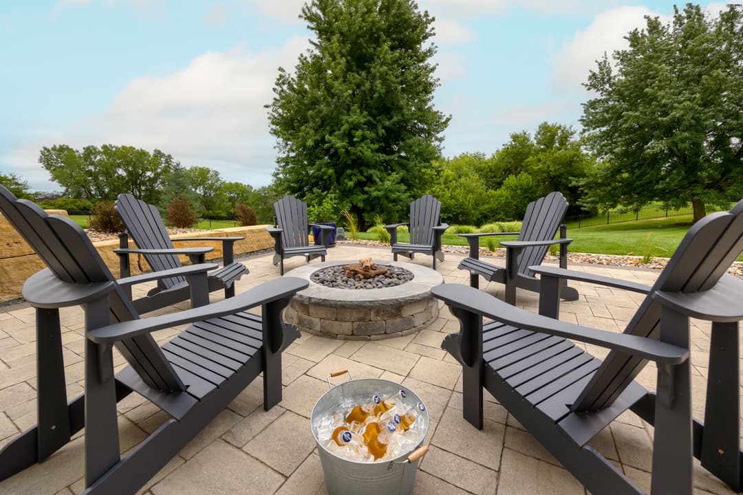 Outdoor patio with black Adirondack chairs surrounding a stone fire pit and bucket of beverages.