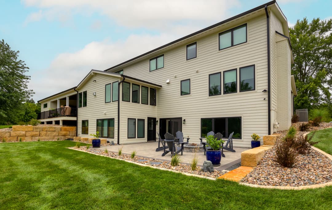 Modern two-story house with a patio, lush lawn, and landscaped garden in a serene setting.