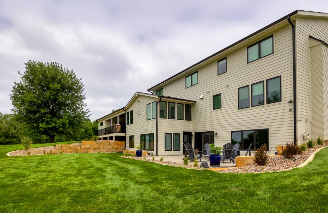Modern two-story home with large windows, landscaped yard, and outdoor seating area.
