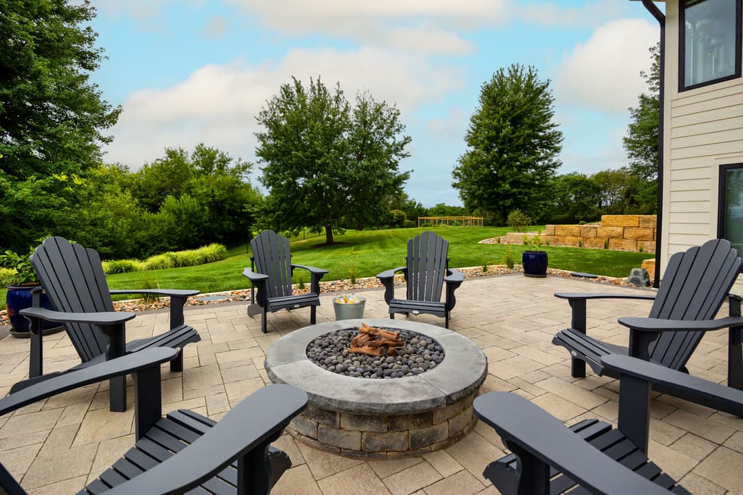 Cozy outdoor patio with black Adirondack chairs surrounding a fire pit in a lush garden.