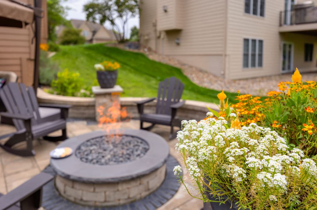 Cozy outdoor fire pit with seating, surrounded by vibrant flowers and a lush green lawn.