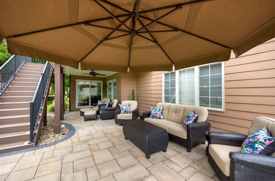 Cozy outdoor patio with sectional sofa, coffee table, and large umbrella in residential setting.