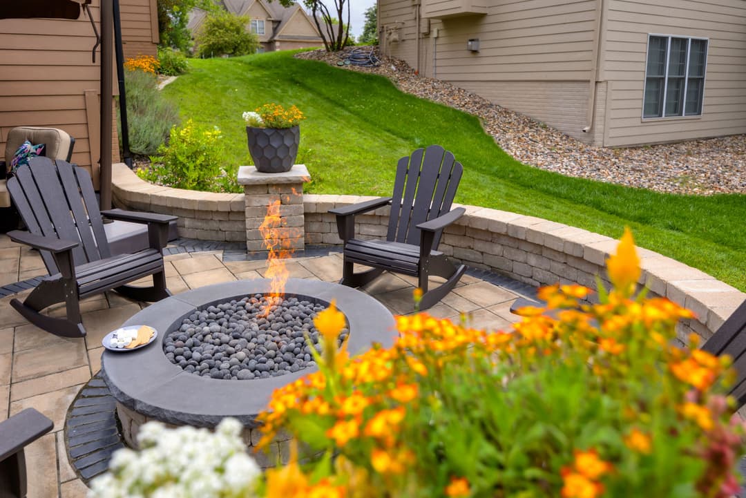 Cozy outdoor fire pit with stone seating, surrounded by flowers and green lawn.