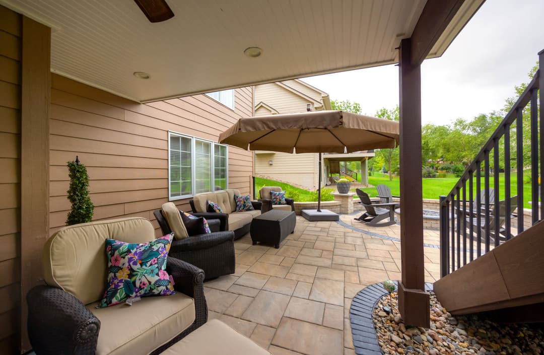 Cozy outdoor patio with comfortable seating, umbrella, and lush green lawn. Perfect for relaxation.