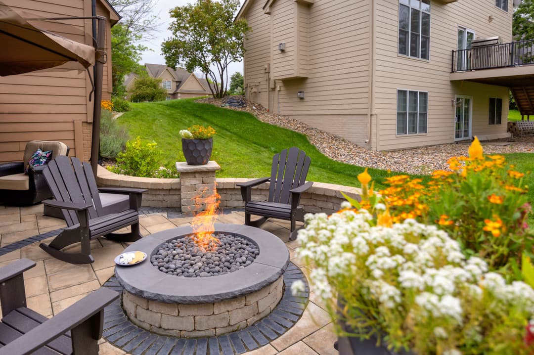 Backyard fire pit surrounded by chairs and colorful flowers in a serene residential setting.