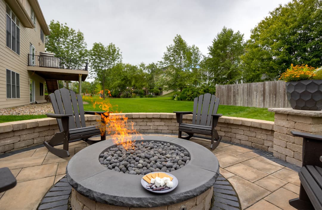 Cozy outdoor fire pit with seating, surrounded by lush greenery and a stone patio.