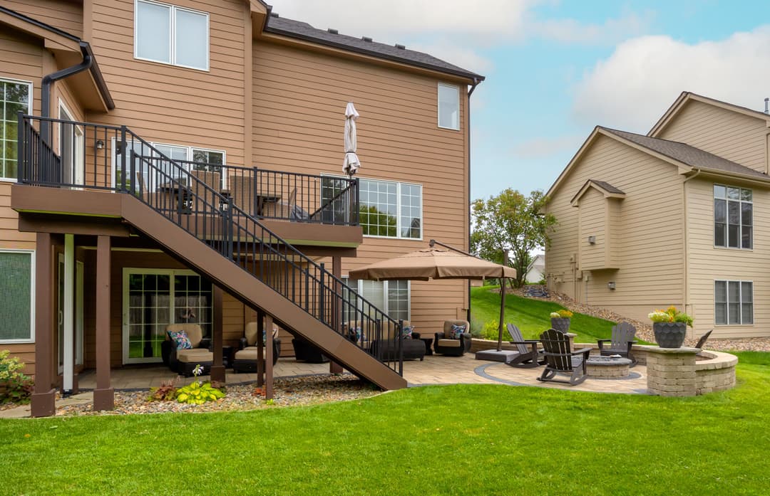 Backyard patio with seating area, stairs, and landscaped garden near a two-story home.