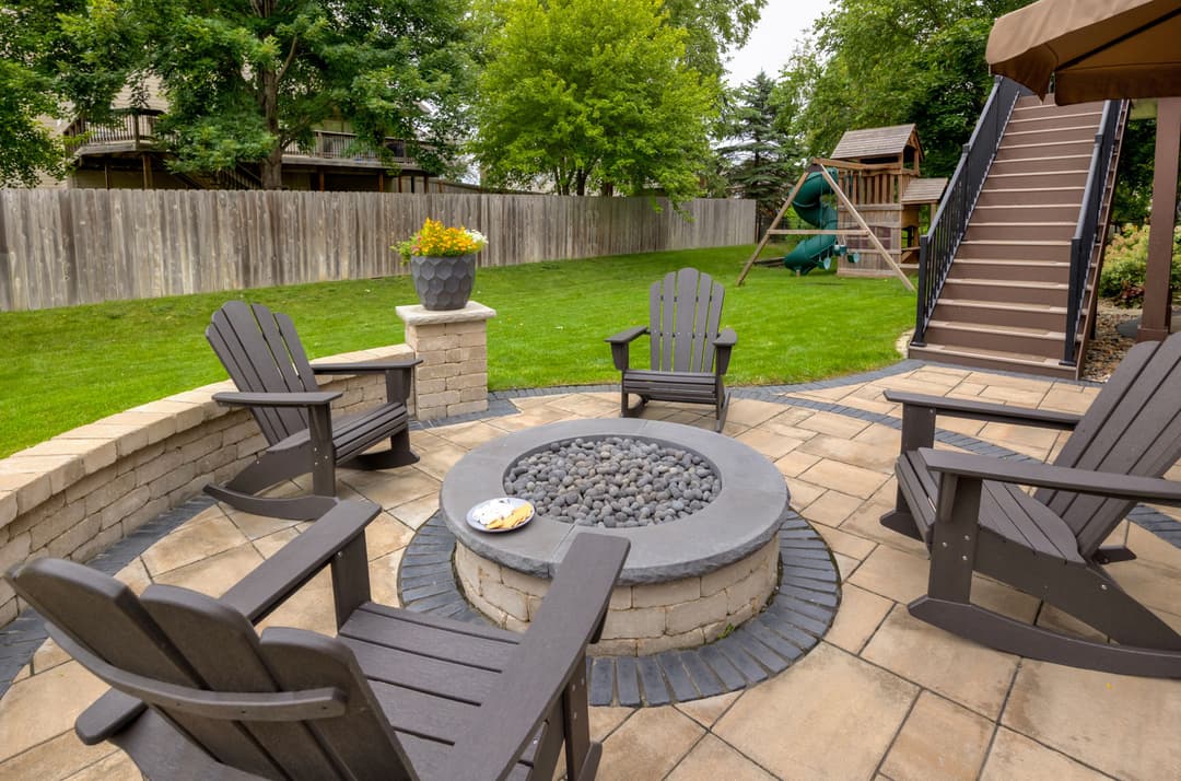 Cozy backyard seating area with fire pit, stone wall, and lush green lawn. Perfect for gatherings.