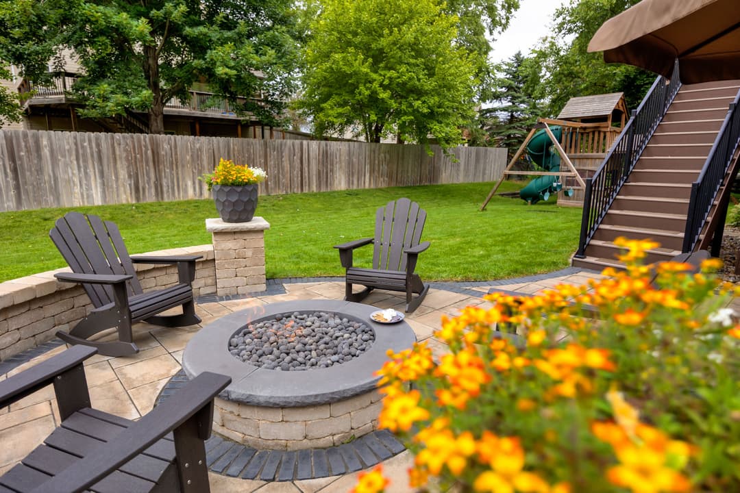 Cozy backyard fire pit surrounded by Adirondack chairs and vibrant flowers in a lush garden.