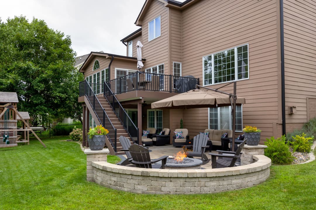 Backyard with fire pit, outdoor seating, and a two-story brown house with a deck.