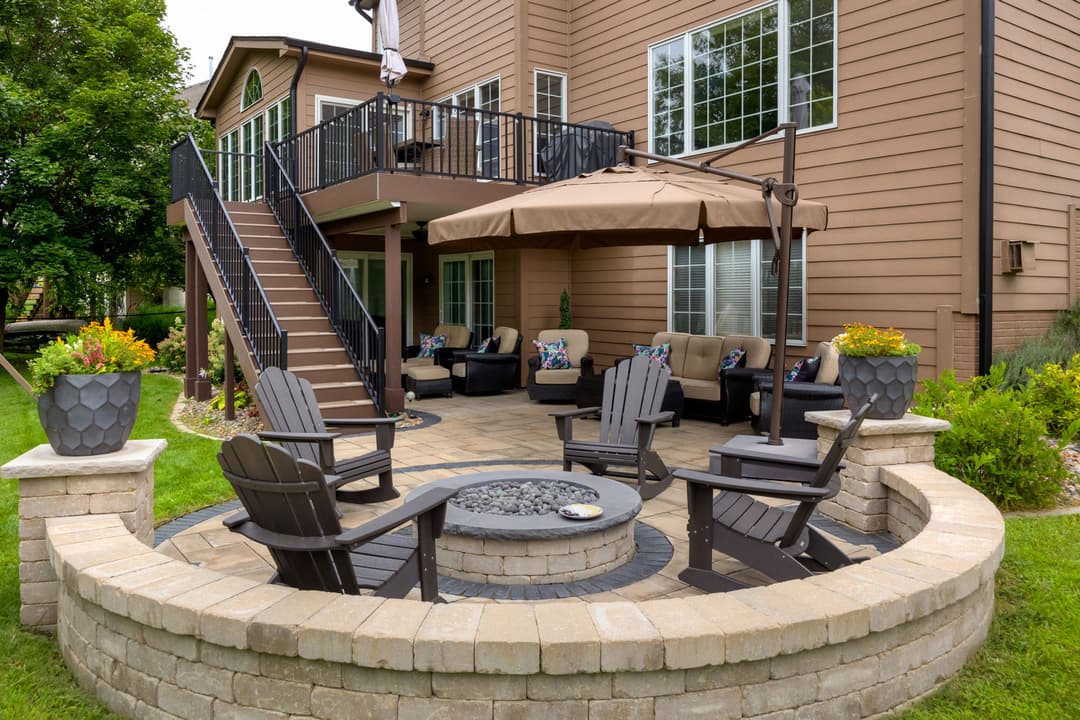 Cozy outdoor patio with seating, fire pit, and shaded area by a stylish home.