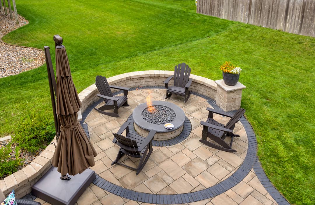 Cozy outdoor patio with fire pit, seating area, and lush green lawn in a serene backyard.