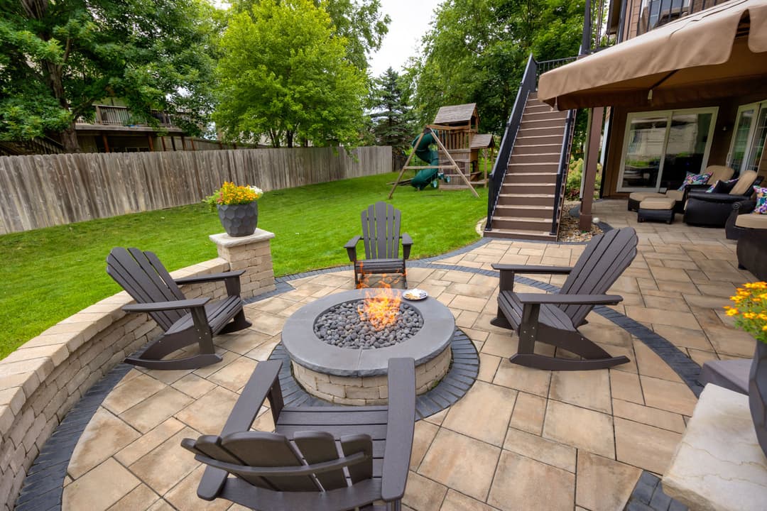 Cozy backyard fire pit surrounded by Adirondack chairs and lush greenery. Perfect for gatherings.