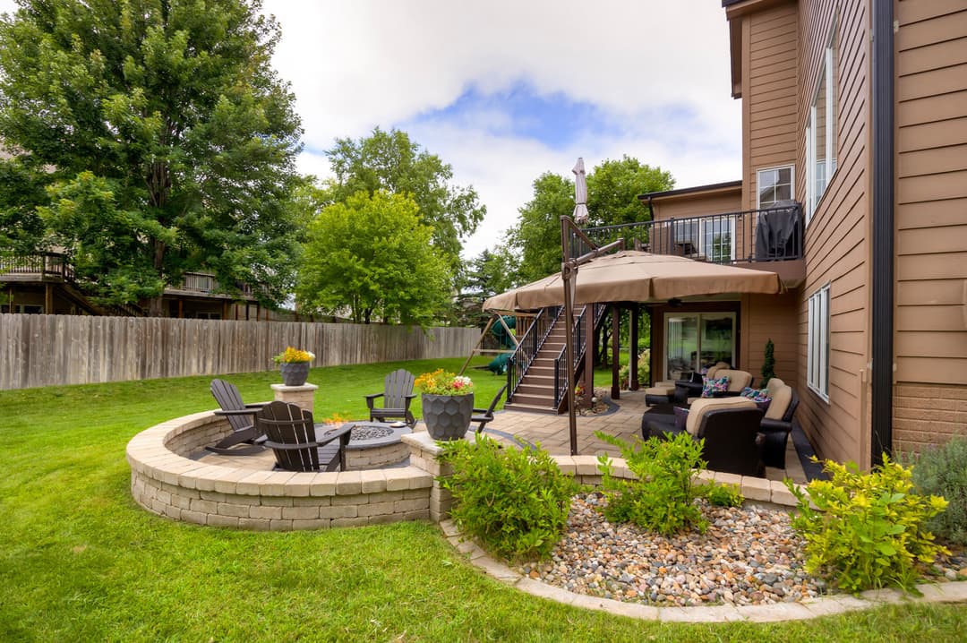Backyard patio with seating area, garden, and trees, featuring a modern home in the background.