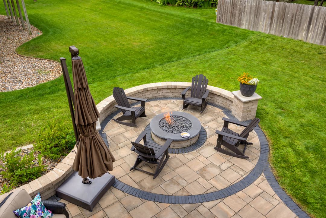 Elegant outdoor patio with fire pit, Adirondack chairs, and sunny green lawn.