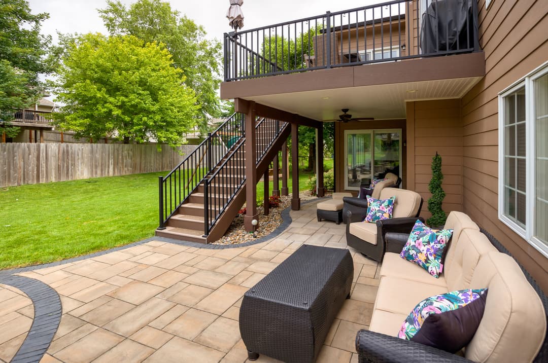 Spacious backyard patio with seating, stairs, and lush green lawn. Ideal for relaxation.