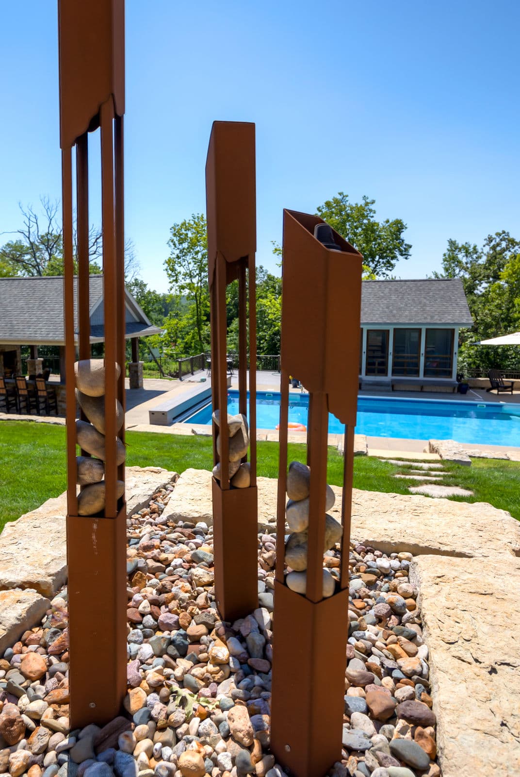 Modern yard sculptures beside a pool, featuring metal frames with decorative stones.