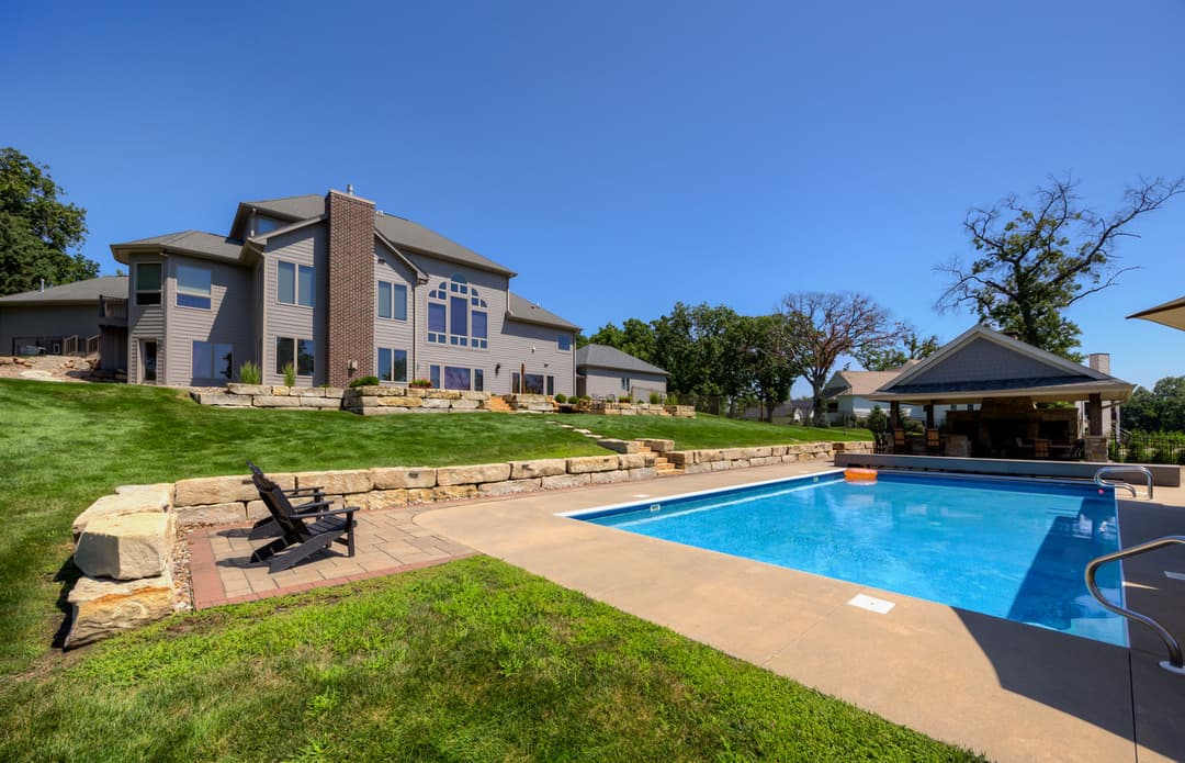 Luxury home with a swimming pool, patio, and landscaped yard under a clear blue sky.